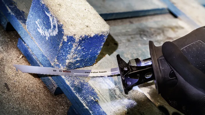 Une personne portant un équipement de sécurité coupe une palette en bois avec une scie alternative.