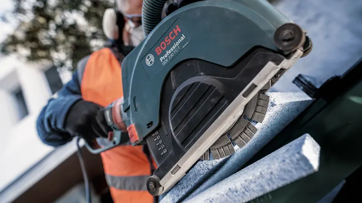 Une personne portant un équipement de sécurité utilise une scie électrique pour couper une dalle de pierre.