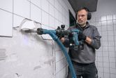 Une personne portant un équipement de sécurité utilise un marteau de démolition sans fil pour casser des carreaux muraux.
