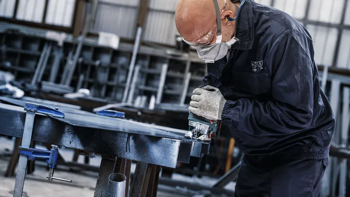 Une personne portant un équipement de sécurité utilise une scie électrique pour couper du métal dans un atelier.