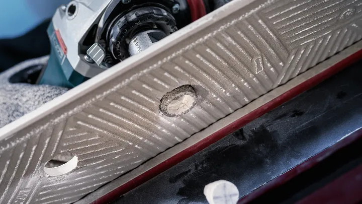 Une personne portant un équipement de sécurité perce un trou dans une tuile avec un outil électrique.