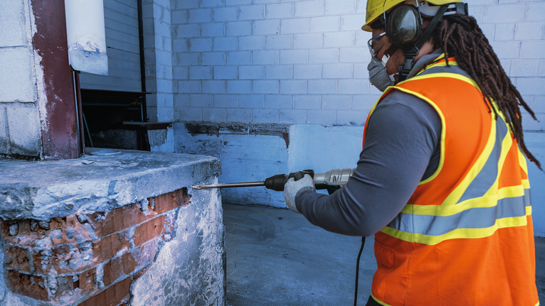 Une personne portant un équipement de sécurité perce un mur en béton sur un chantier de construction.