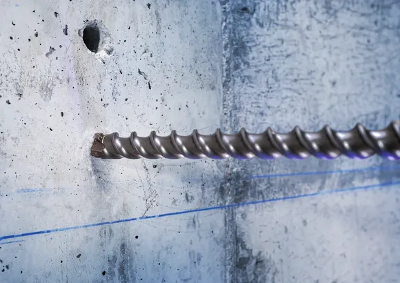 Grande mèche à maçonnerie perçant un mur en béton.