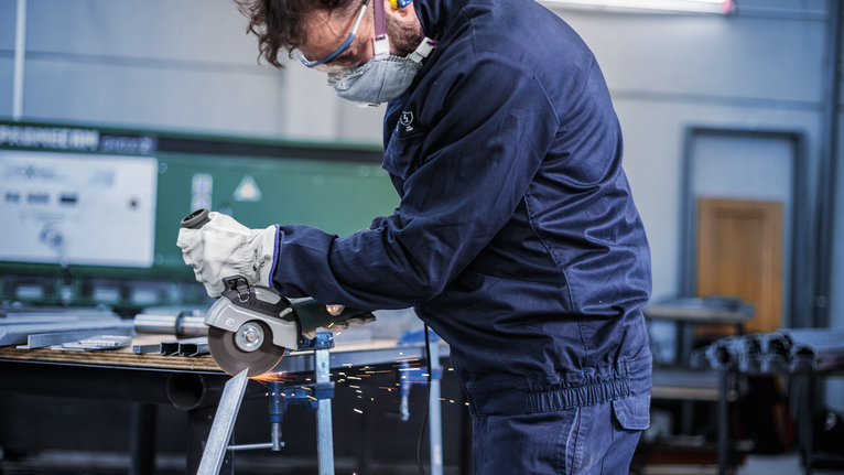 Une personne portant un équipement de sécurité utilise une meuleuse d’angle pour couper du métal, produisant des étincelles.