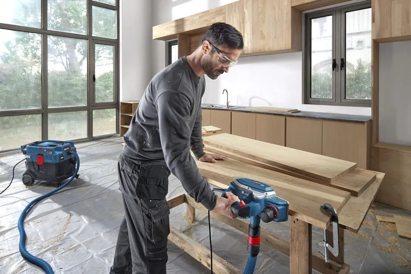Une personne portant un équipement de sécurité utilise une raboteuse sur des planches de bois dans un atelier.