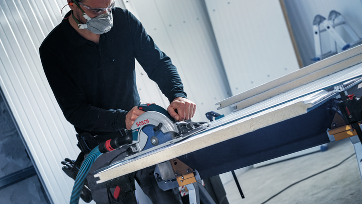 Une personne portant un équipement de sécurité coupe une planche avec une scie circulaire sur une table de travail.