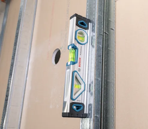 Niveau à bulle aligné contre un panneau de plaques de plâtre comportant une découpe.