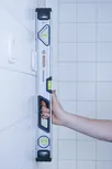 Personne tenant un niveau à bulle contre un mur carrelé.