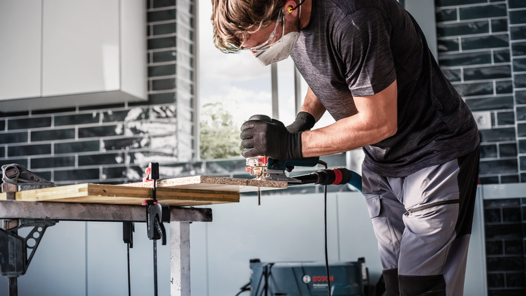 Une personne portant un équipement de sécurité utilise une scie sauteuse pour couper du bois sur un établi.
