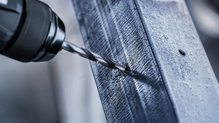 Une perceuse électrique crée un trou dans une poutre métallique.