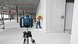 Лазерное устройство Bosch Professional на штативе, рабочий отмечает стену.