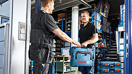 Два чоловіки передають синю коробку інструментів Bosch Professional, майстерня.