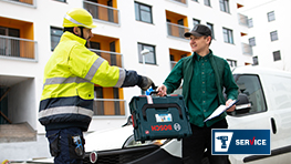 A worker in protective clothing hands a toolbox to a man.