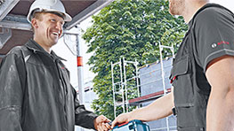 Two men in work clothes shake hands at a construction site.