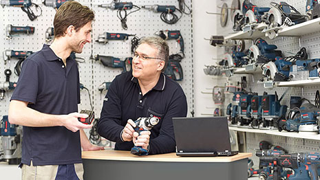 Двама мъже в униформи обсъждат инструменти Bosch пред рафт.