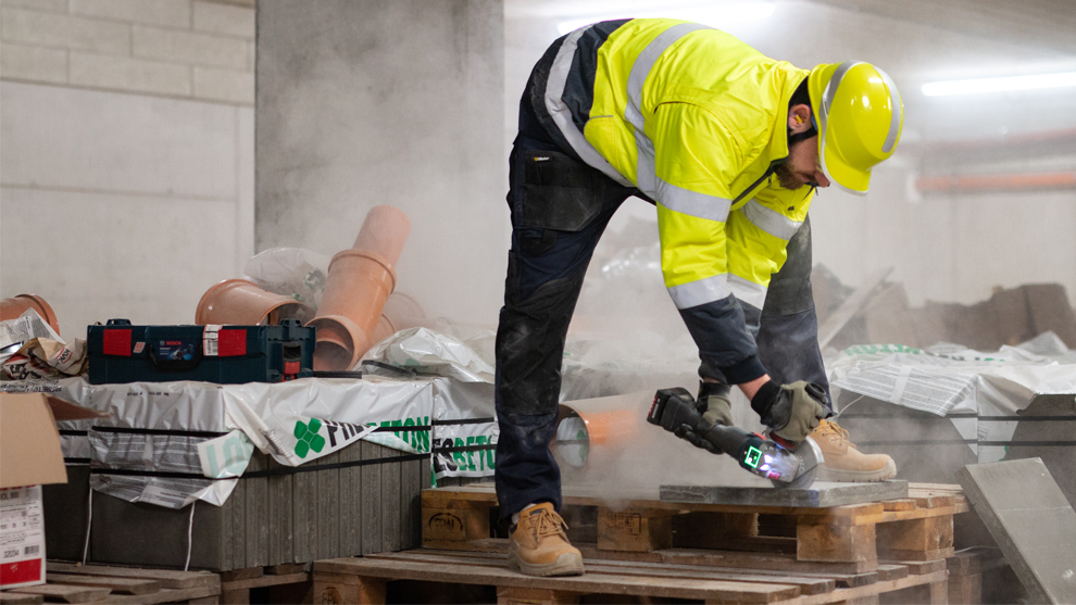 Рабочий в желтой предупредительной жилетке режет камни инструментом Bosch.