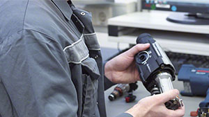 Muž drží v ruce nástroj Bosch Professional, obklopen nářadím.