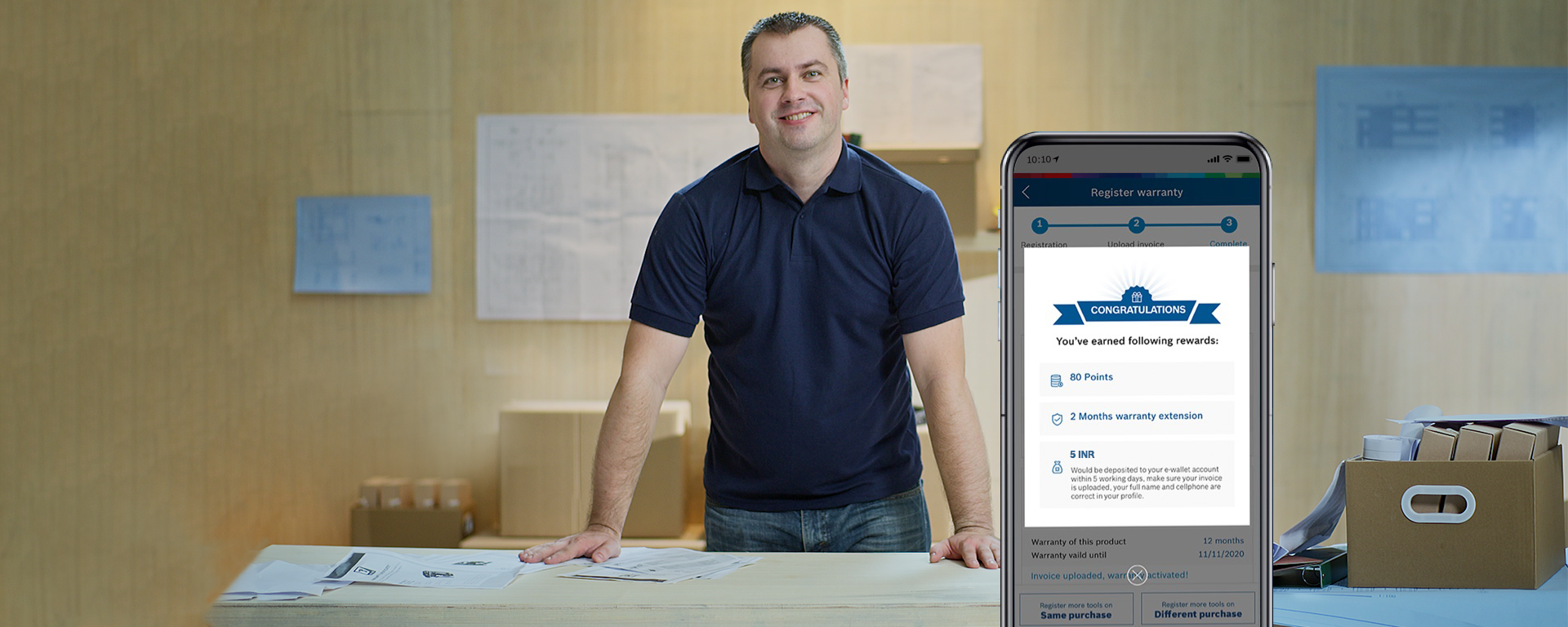 A man in a blue shirt stands at a table with papers and a phone.