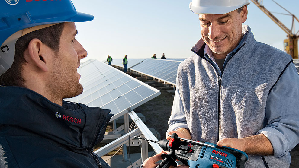 Two men in a solar field are holding Bosch tools in their hands.