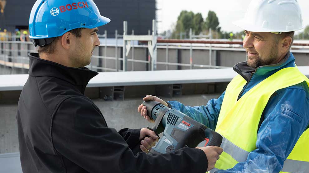 Two construction workers are exchanging a Bosch Professional tool on a construction site.