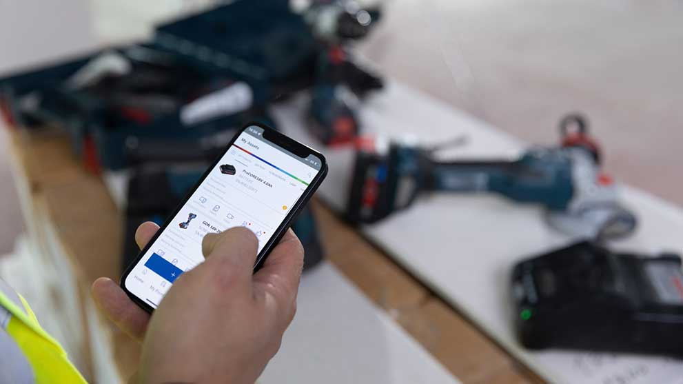 A person is holding a smartphone and looking at the Bosch app. Tools in the background.