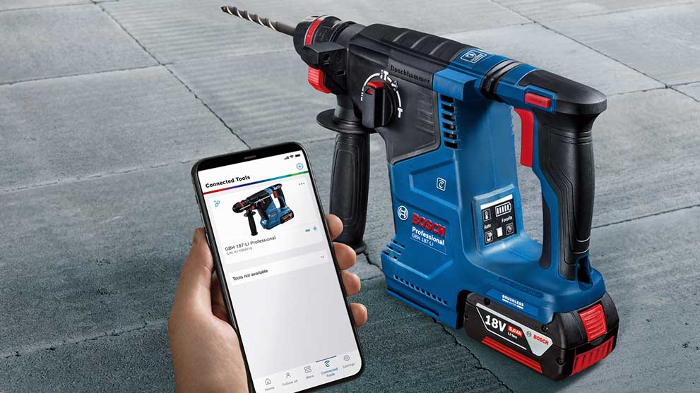 Bosch Professional cordless hammer drill stands on concrete floor next to a smartphone.