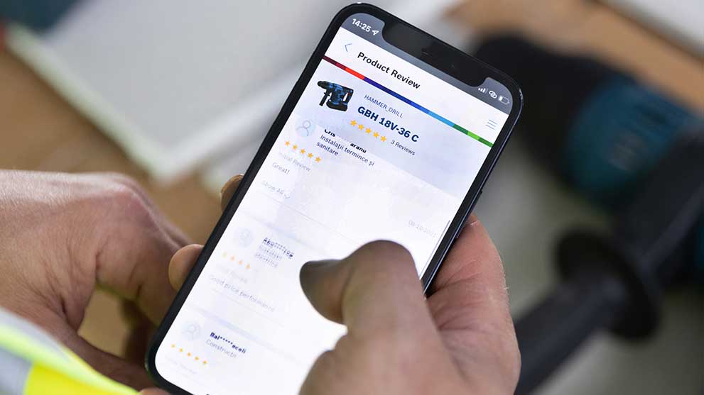 A hand holds a smartphone with reviews for Bosch hammer drills.