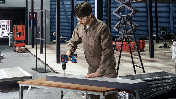 رجل يستخدم مثقاب يعمل على لوح رمادي في ورشة عمل.