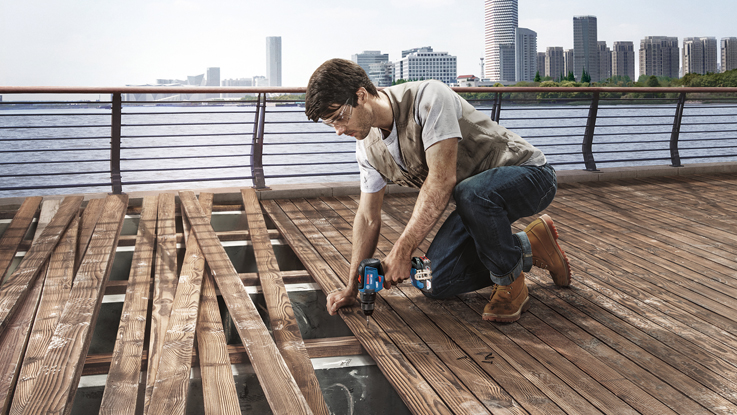 رجل يستخدم أداة كهربائية لاسلكية زرقاء من بوش بروفيشينال لتركيب ألواح خشبية.