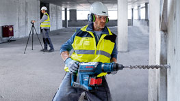 Рабочий с дрелью в желтом жилете безопасности сверлит стену.