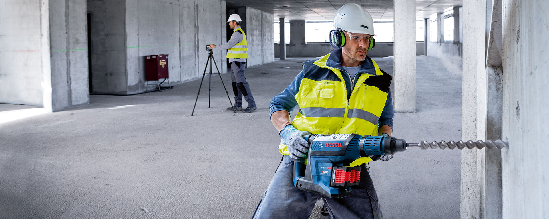 A worker with a Bosch hammer drill is drilling into a concrete wall.