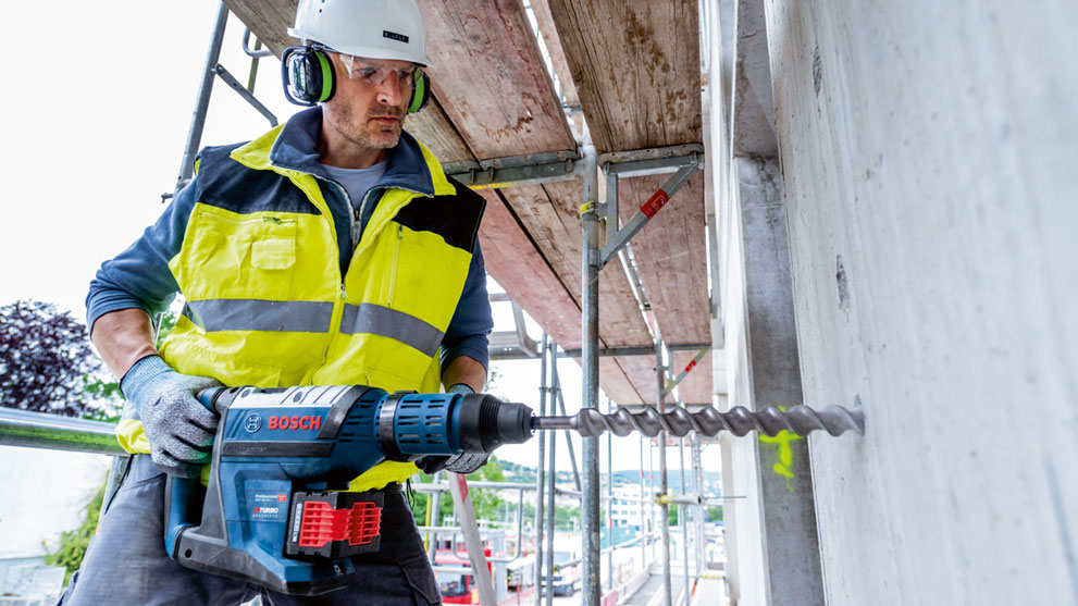 Рабочий с дрелью Bosch сверлит стену на строительных лесах.