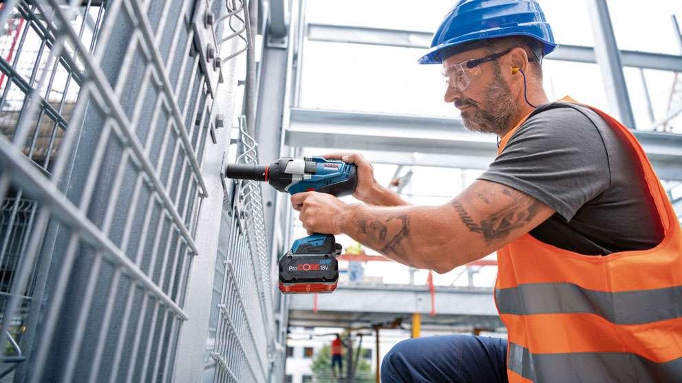 Мужчина в оранжевом жилете использует синий аккумуляторный шуруповерт Bosch.