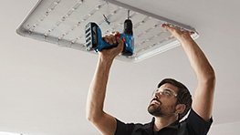 Мужчина устанавливает лампу с помощью синего аккумуляторного шуруповерта Bosch.