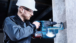 Мужчина в каске сверлит стену синим инструментом Bosch Professional.