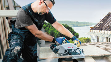 Ремесленник режет дерево с помощью циркулярной пилы Bosch на улице.