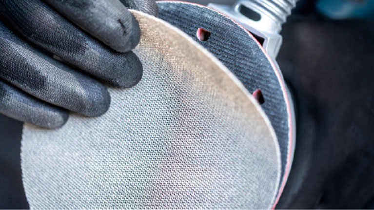 Дві руки в чорних рукавичках тримають шліфувальний диск.