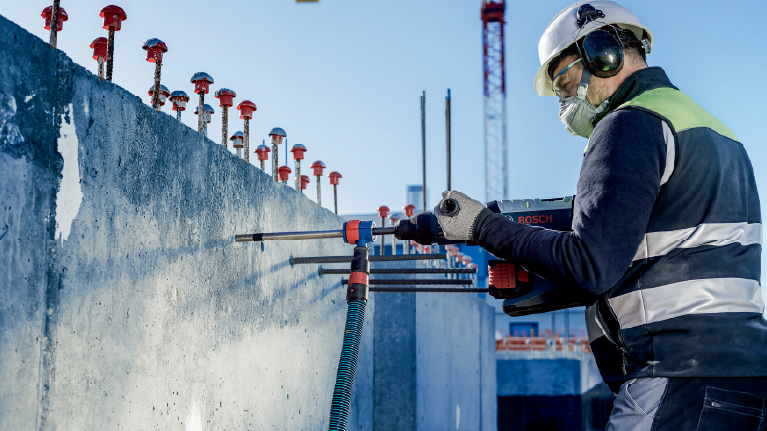 Робітник з інструментами Bosch працює над бетонною стіною на будівельному майданчику.