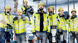 Шест будівельників у жовтих шоломах і жилетах безпеки стоять на будівельному майданчику.