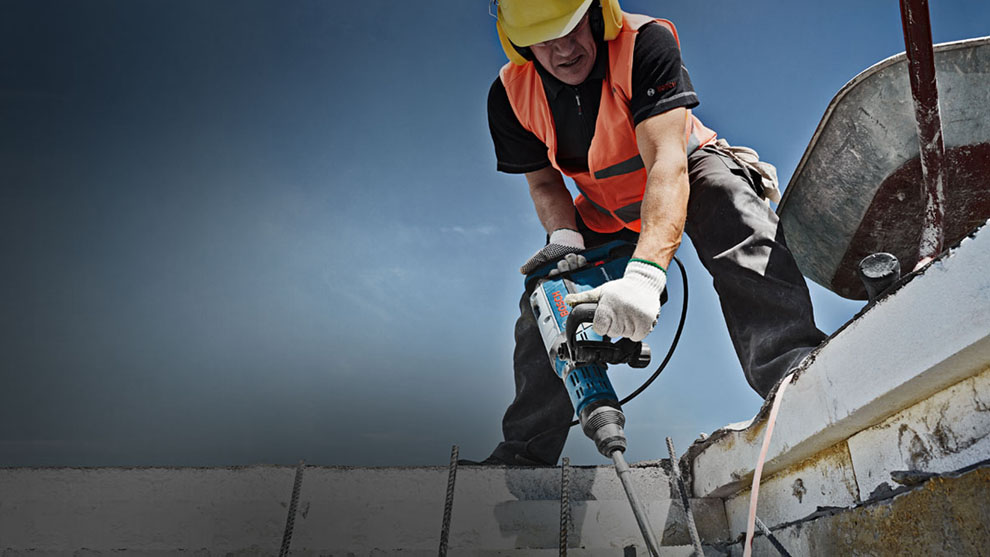 Работник с предупредителна жилетка и бормашина Bosch на строителната площадка.