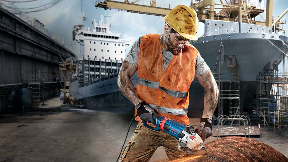 Delavec s zaščitno čelado reže kovino z modro Bosch napravo.