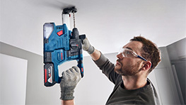 Мужчина в защитных очках использует синий аккумуляторный гвоздезабиватель Bosch на потолке.