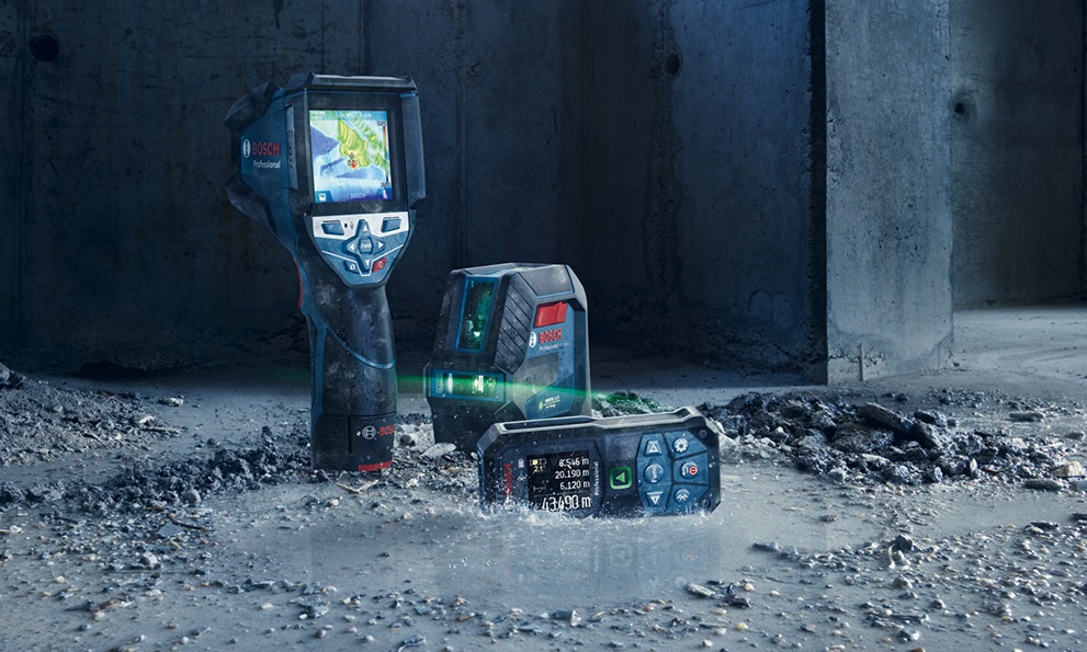 Tři zařízení Bosch Professional stojí na šedém, vlhkém povrchu.