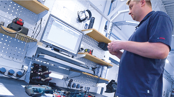 Muž stojí u stolu s nástroji Bosch a počítačem.