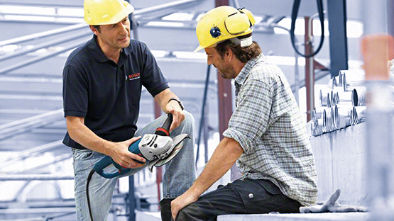 Dva muži v helmách kontrolují nástroj Bosch na staveništi.