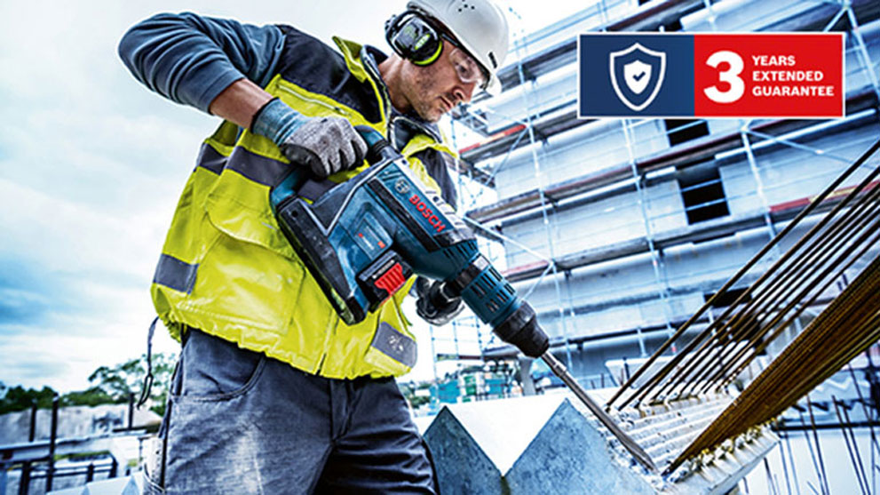 Mężczyzna w żółtej koszuli ochronnej używa wiertarki Bosch na placu budowy.