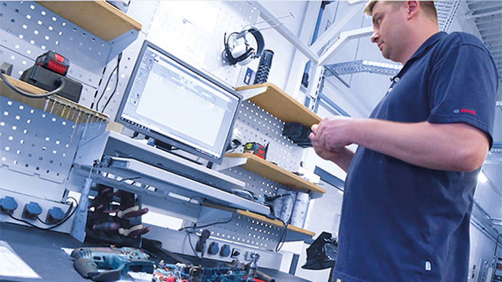 Mężczyzna stoi przy stole z narzędziami Bosch i komputerem.