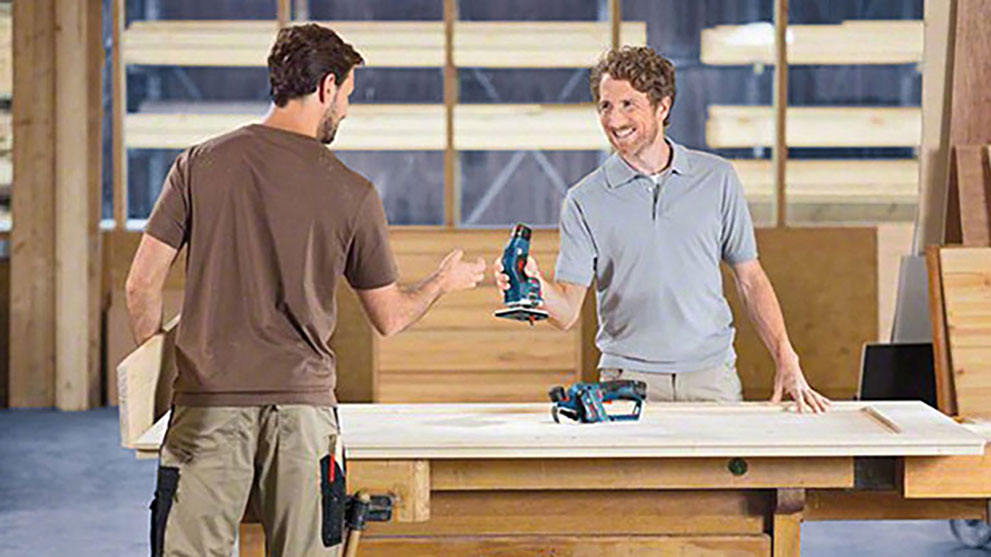 Dwaj mężczyźni w warsztacie przekazują sobie narzędzia Bosch na stole.