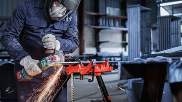 A worker wearing a safety helmet is cutting metal with a Bosch Professional machine.