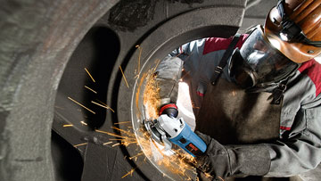 A craftsman in protective clothing is cutting metal with a blue Bosch machine.